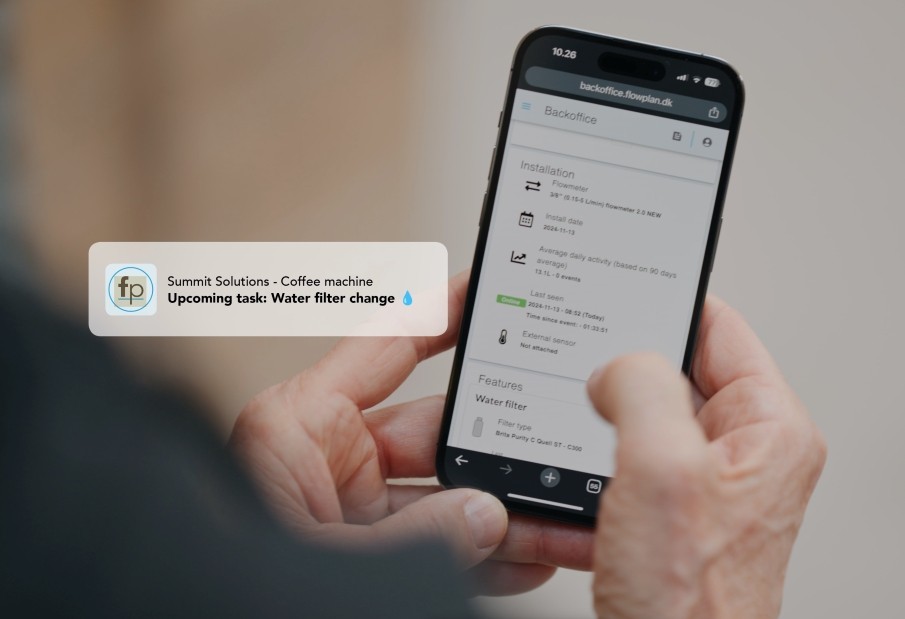 A phone showing Flowplan's backoffice with an upcoming water filter change on a coffee machine