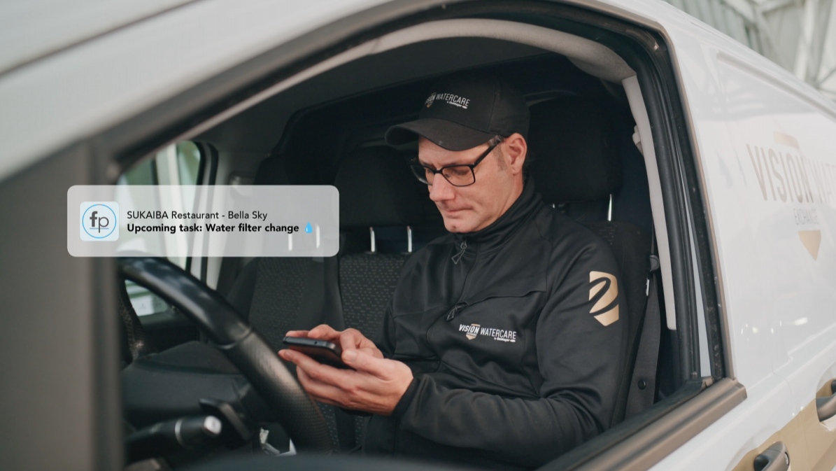 A service technician in a van reading an upcoming water filter change for a restaurant