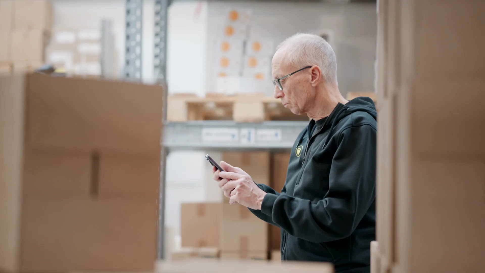A warehouse worker checking stock on a phone between the shelves